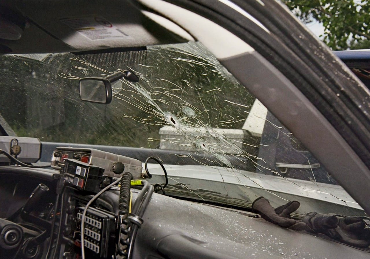 default-516 View from the inside of the dashboard and windshield of a police vehicle, with bullet holes and cracked glass.